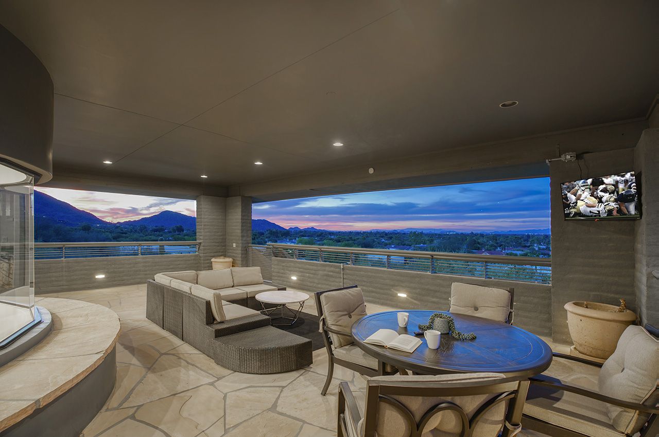 Luxury 5-bedroom vacation home balcony with panoramic mountain and city views, outdoor seating, and a TV at dusk.