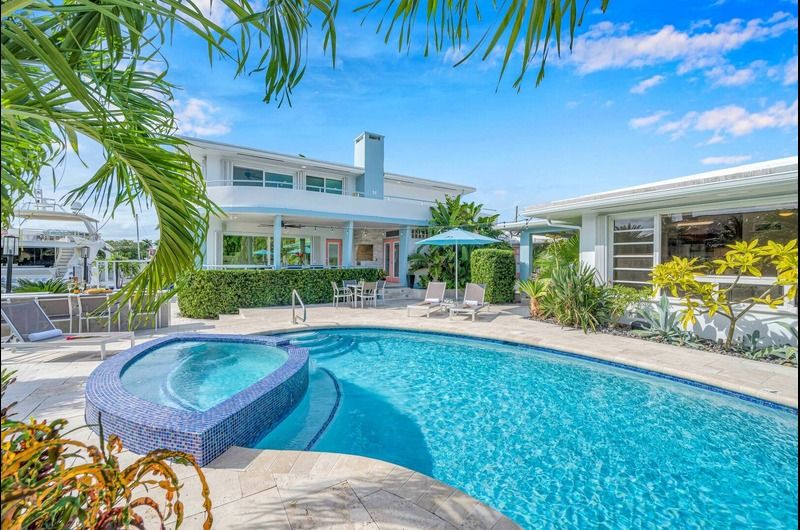 Luxury Fort Lauderdale vacation home with a pool, hot tub, outdoor seating, and tropical landscaping.