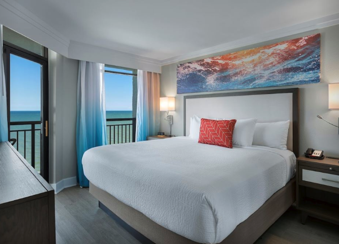 Grande Cayman Resort Modern hotel room with a large bed, ocean view through glass doors, colorful artwork, and contemporary decor at Grande Cayman Resort.