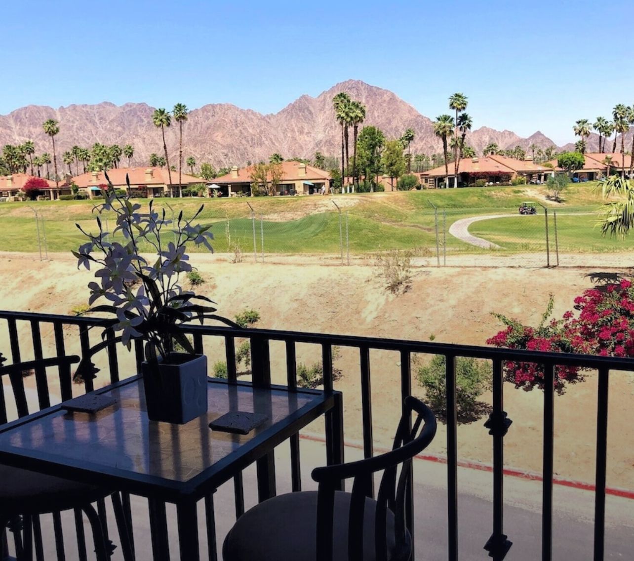 Peaceful Retreat with Mountain/Golf course Views, No Pets Balcony view of a golf course with mountains in the background, featuring a table with a potted plant and chairs, peaceful and scenic.