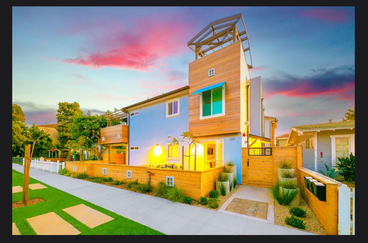 Modern beach condo in Oceanside, CA with colorful exterior, landscaped yard, and sunset sky, near ocean and attractions.
