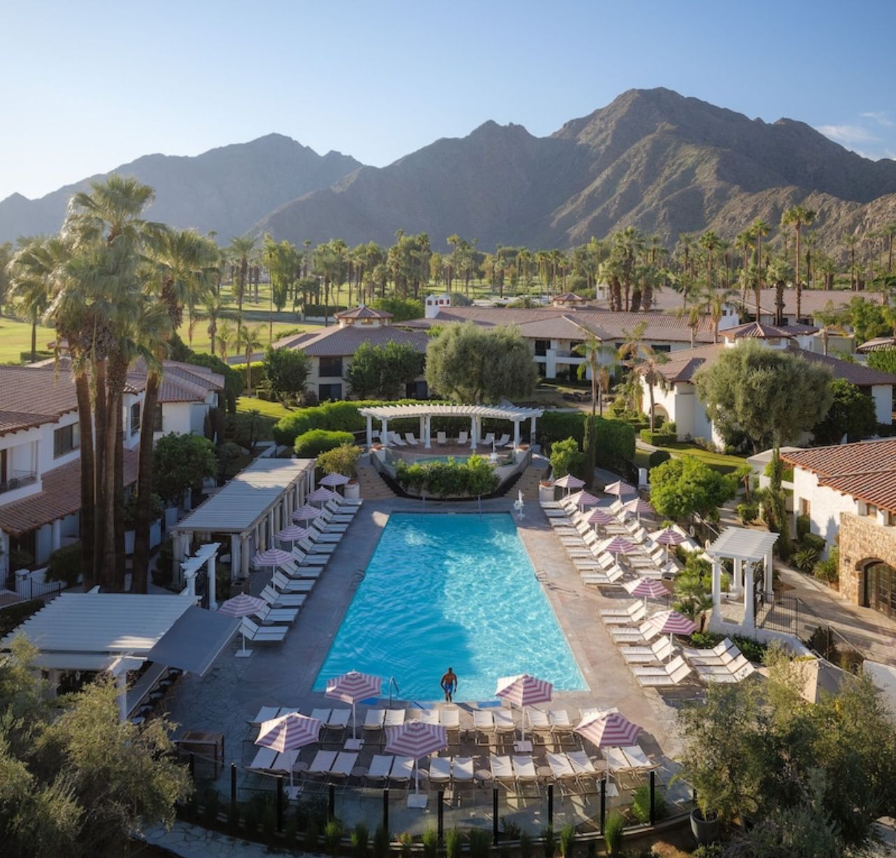 Tommy Bahama Miramonte Resort & Spa A luxurious resort pool area surrounded by lounge chairs, umbrellas, lush greenery, palm trees, and mountain views.