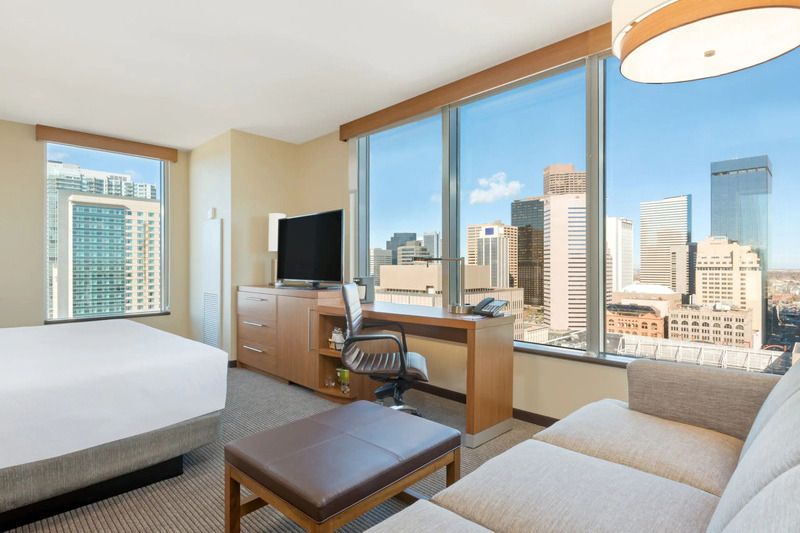 Luxurious hotel room at Hyatt Place Denver Downtown with large windows offering city skyline views, modern furniture, and a workspace.
