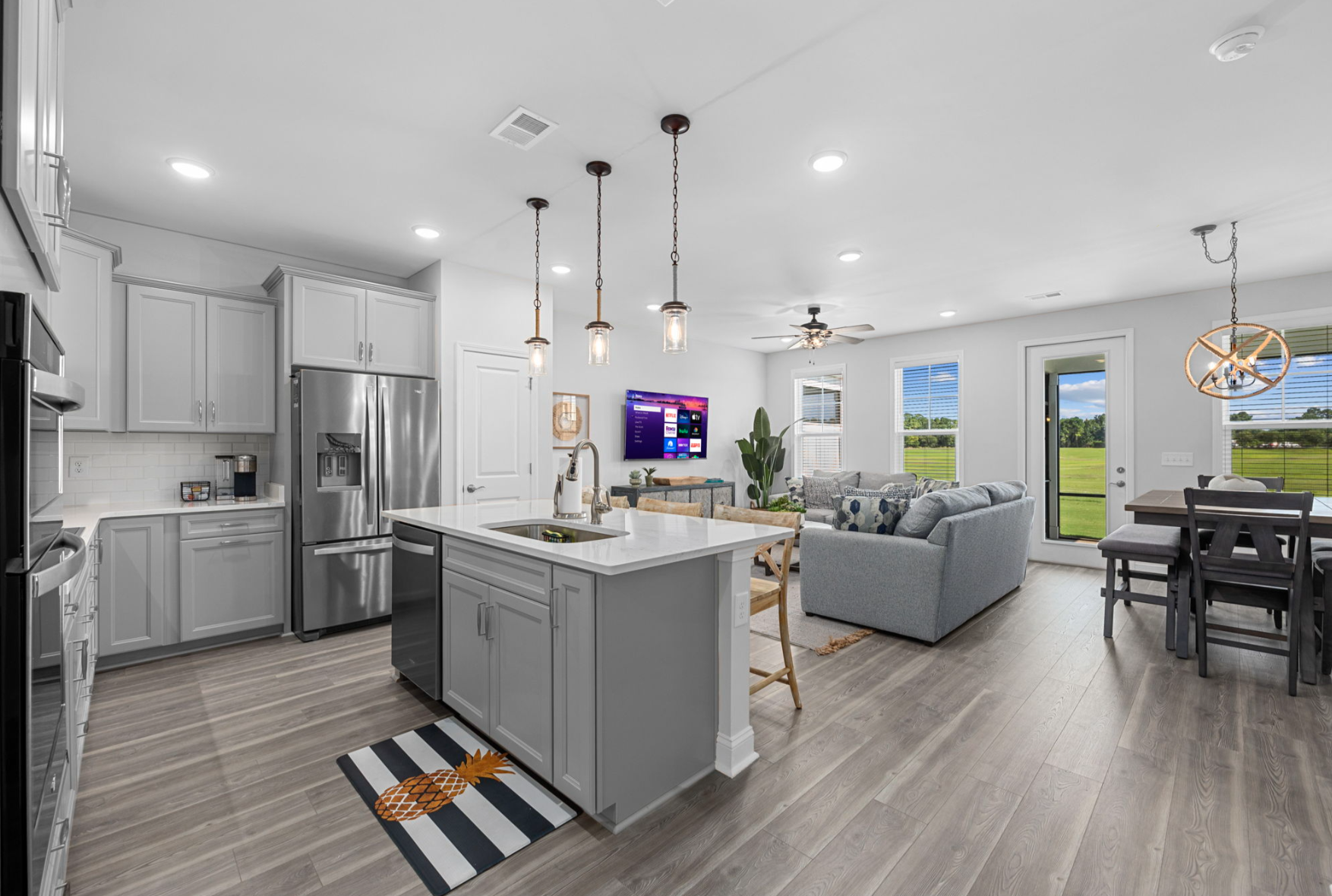 Barefoot Getaway I Bright, modern open-concept kitchen and living room with gray cabinets, stainless steel appliances, and large windows showing a green outdoor view.
