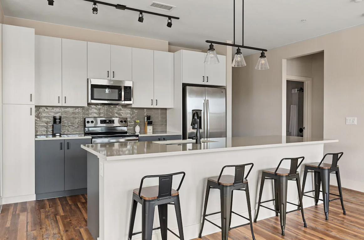 Modern kitchen with white and gray cabinets, stainless steel appliances, and a breakfast bar with four black chairs.