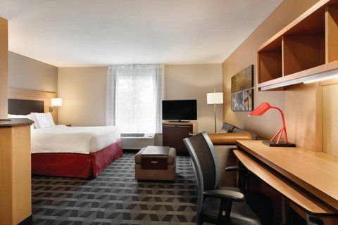 Interior of a hotel room at TownePlace Suites Denver DTC featuring a bed, desk, TV, and cozy seating area.