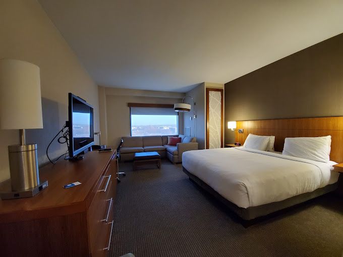Modern hotel room at Hyatt Place Cherry Creek with a large bed, flat-screen TV, sofa, and city view through the window.