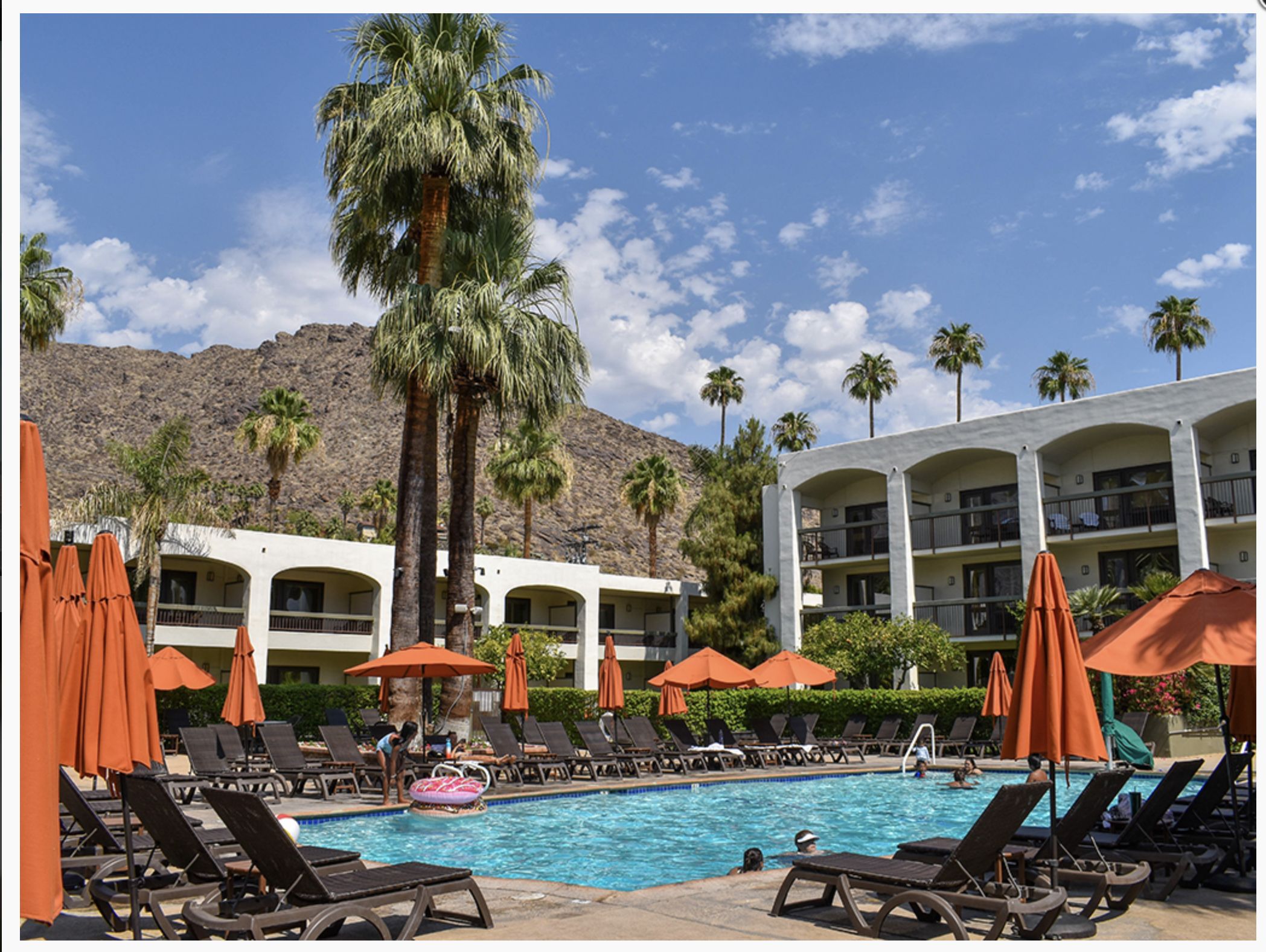 PALM MOUNTAIN RESORT & SPA Luxury pool area at Palm Mountain Resort & Spa with orange umbrellas, lounge chairs, palm trees, and mountain backdrop.