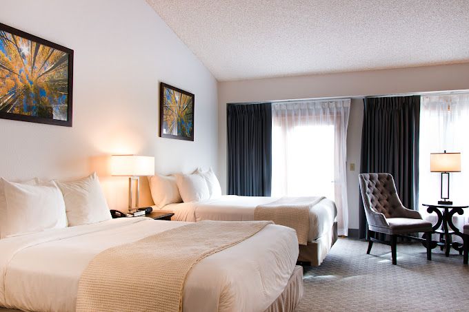 Luxurious hotel room at Lone Tree Golf Club & Hotel with two beds, modern decor, and natural light from large windows.
