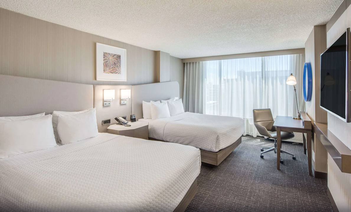 Modern hotel room at Sonesta Denver Downtown with two beds, a work desk, and large window with sheer curtains.