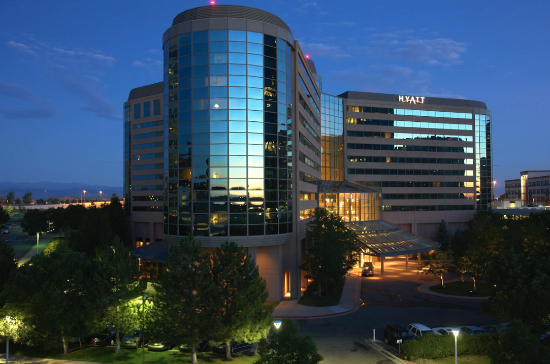 Night view of the Hyatt Regency Denver Tech Center building with illuminated windows and a parking lot surrounded by trees.