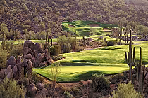 Scenic golf course at Sunridge Canyon with lush green fairways, desert rocks, and tall cacti in a desert landscape.