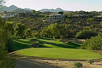 Desert Canyon golf course with lush green fairways, sand traps, surrounded by trees and desert landscape, mountains in the background.