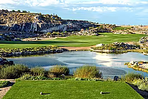 Scenic golf course at Verrado Golf Club with lush green fairways, water hazards, and rocky hills under a blue sky.