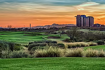 Scenic view of Whirlwind Golf Club in Arizona at sunset, featuring lush green fairways, sand traps, and a modern building in the background.