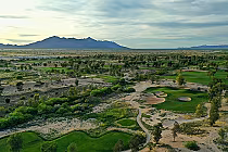 Aerial view of Southern Dunes golf course in Arizona with lush green fairways, sand traps, trees, and distant mountains under a cloudy sky.