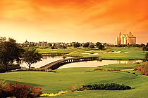 Reunion Resort's Watson Course features lush green fairways, a water hazard, and scenic buildings under a vibrant sunset sky.