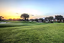 Scenic view of TPC Tampa Bay golf course at sunset with lush green fairways, trees, and a clubhouse in the background.