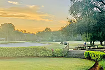 Scenic view of Carrollwood Country Club golf course at sunset with lush greenery, trees, and a golf cart in the distance.
