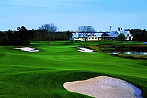 Scenic view of Southern Dunes Golf Club with lush green fairways, sand bunkers, water hazards, and a clubhouse in the background.
