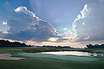 Scenic view of RTJ The Shoals Schoolmaster Course golf course with lush green fairways, a water hazard, and dramatic cloud-filled sky.