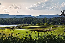 Scenic view of the RTJ Silver Lakes Short Course golf course with lush green fairways, water hazards, and distant mountains under a partly cloudy sky.