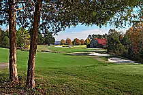 Luxurious golf course at RTJ Hampton Cove Highlands, featuring lush green fairways, sand bunkers, and a rustic barn surrounded by trees.