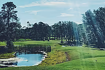Scenic view of Hidden Hills Golf Club in Jacksonville featuring lush green fairways, trees, a water hazard, and a bright blue sky.