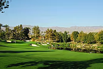 Beautiful view of the Indian Wells Players Course with lush green fairways, sand bunkers, trees, and a water hazard, set against distant mountains.