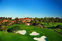 Aerial view of The Grand Golf Club in San Diego featuring lush green golf course, sand bunkers, trees, and a large clubhouse under a clear blue sky.