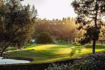 Golf course with green, flag, trees, and water hazard at sunset, showcasing the scenic 18th hole at Rancho Bernardo Inn.