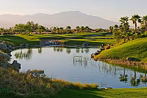 Scenic golf course with lush green fairways, palm trees, water hazards, and mountains in the background at Eagle Falls.