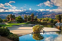 Scenic view of Firecliff golf course at Desert Willow Golf Resort with lush greenery, palm trees, water features, and mountains in the background.