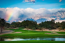 Scenic view of a golf course at Desert Willow Golf Resort with lush green fairways, water hazards, trees, mountains, and a rainbow in the sky.