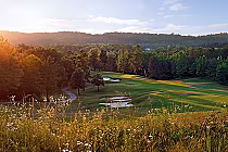 Scenic view of RTJ Oxmoor Valley Valley Course with lush green fairways, sand traps, water hazards, and surrounding trees at sunset.