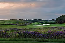 Scenic view of RTJ The Shoals Fighting Joe golf course with lush green fairways, purple flowers, water hazards, and a cloudy sky.