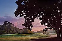 Sunset over a golf course with lush green fairways, water hazards, and large trees, set on former soybean fields in Alabama.