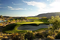 A scenic golf course at sunset with lush green fairways, sand bunkers, water hazards, and desert landscape in Las Vegas.