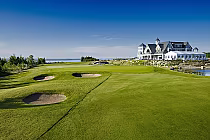 Scenic view of Cobble Beach Golf Links with lush green fairways, sand bunkers, and a large elegant clubhouse overlooking water.