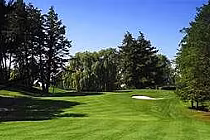 Lush green golf course at Cherry Downs Golf Club with tall trees, sand traps, and a clear blue sky.