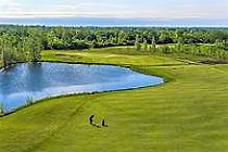 Aerial view of a golf course with a water hazard, lush green fairways, surrounded by trees, under a partly cloudy sky at Loyalist Golf and Country Club.