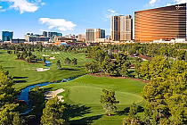 Aerial view of Wynn Golf Club with lush green fairways, sand traps, and water hazards, set against the Las Vegas skyline with tall hotels and buildings.
