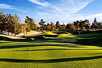 Scenic view of Desert Pines Golf Club in Las Vegas, featuring lush green fairways, sand traps, and trees under a blue sky.