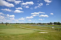 Scenic view of a golf course with green fairways, a water hazard, and a bright blue sky with scattered white clouds in Ontario.