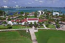 Aerial view of Normandy Shores Golf Course in Miami Beach with lush green lawns, surrounding buildings, and water in the background.