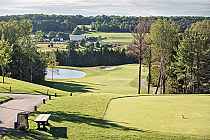 Scenic view of Braestone Club golf course with lush green fairways, trees, a water hazard, and rolling landscape in the background.