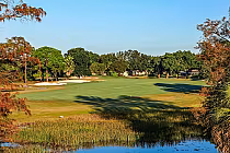 Scenic view of PGA National Resort's Fazio Course with lush green fairways, sand bunkers, and trees under a clear blue sky.