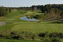 Scenic view of Wyndance Golf Club with lush green fairways, a pond, and rolling hills under a clear sky.