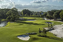 Beautiful view of the PGA National Resort's Staple Course with lush green fairways, sand bunkers, water hazards, and trees under a partly cloudy sky.