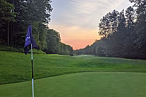 Golf course at sunset with green fairway, flag, and trees, offering a peaceful view of luxury golf in Toronto.